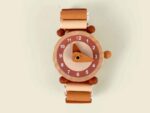 Holzuhr Emma von Egmont Toys mit roséfarbenen Zahlen und elastischem Perlenarmband, zusammen mit weiteren Accessoires arrangiert.